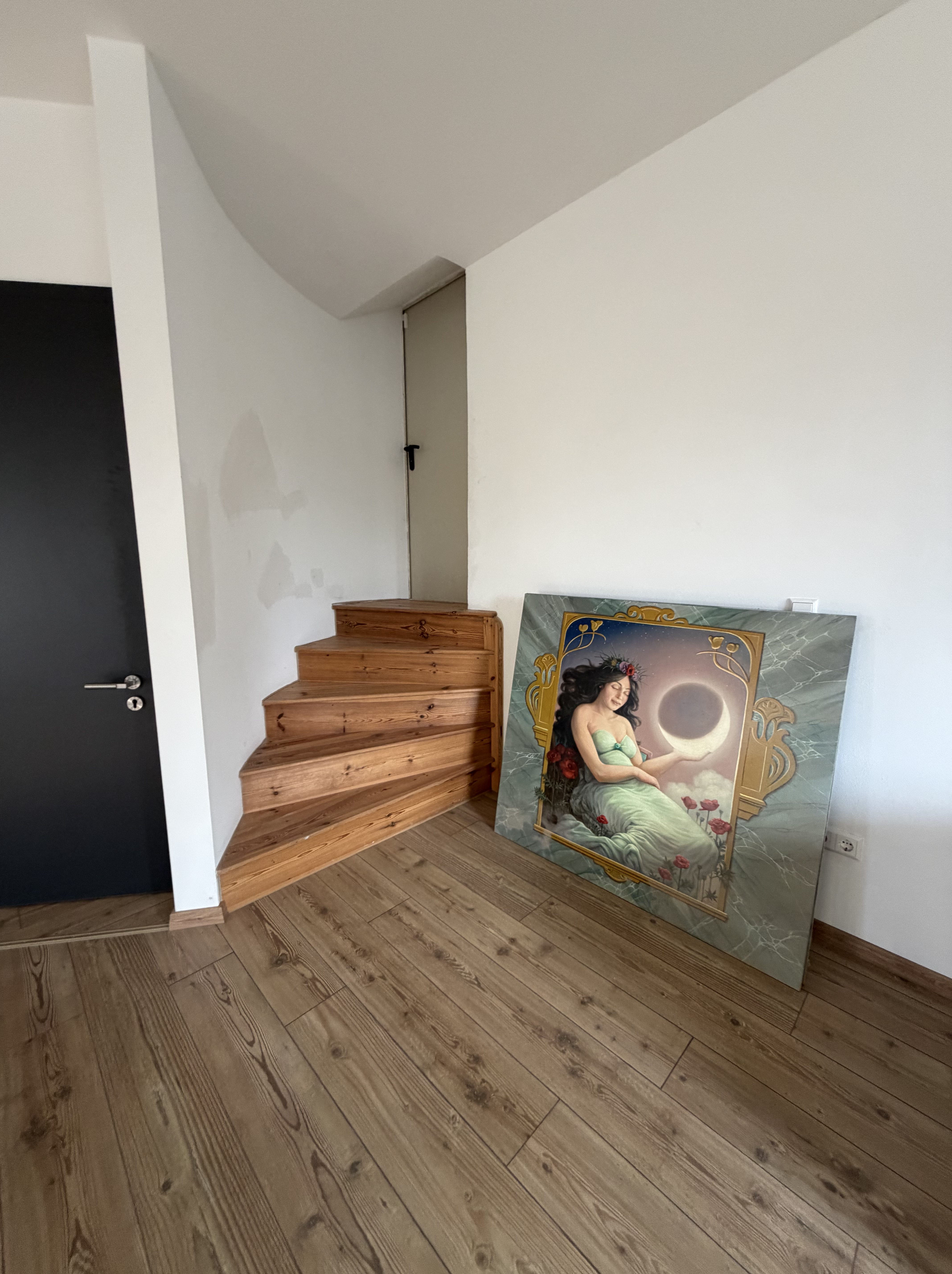 Eine Treppe aus Holz führt nach oben, während ein großes Gemälde einer Frau mit langen, dunklen Haaren und einem Mondmotiv an der Wand in einem modernen Raum steht.