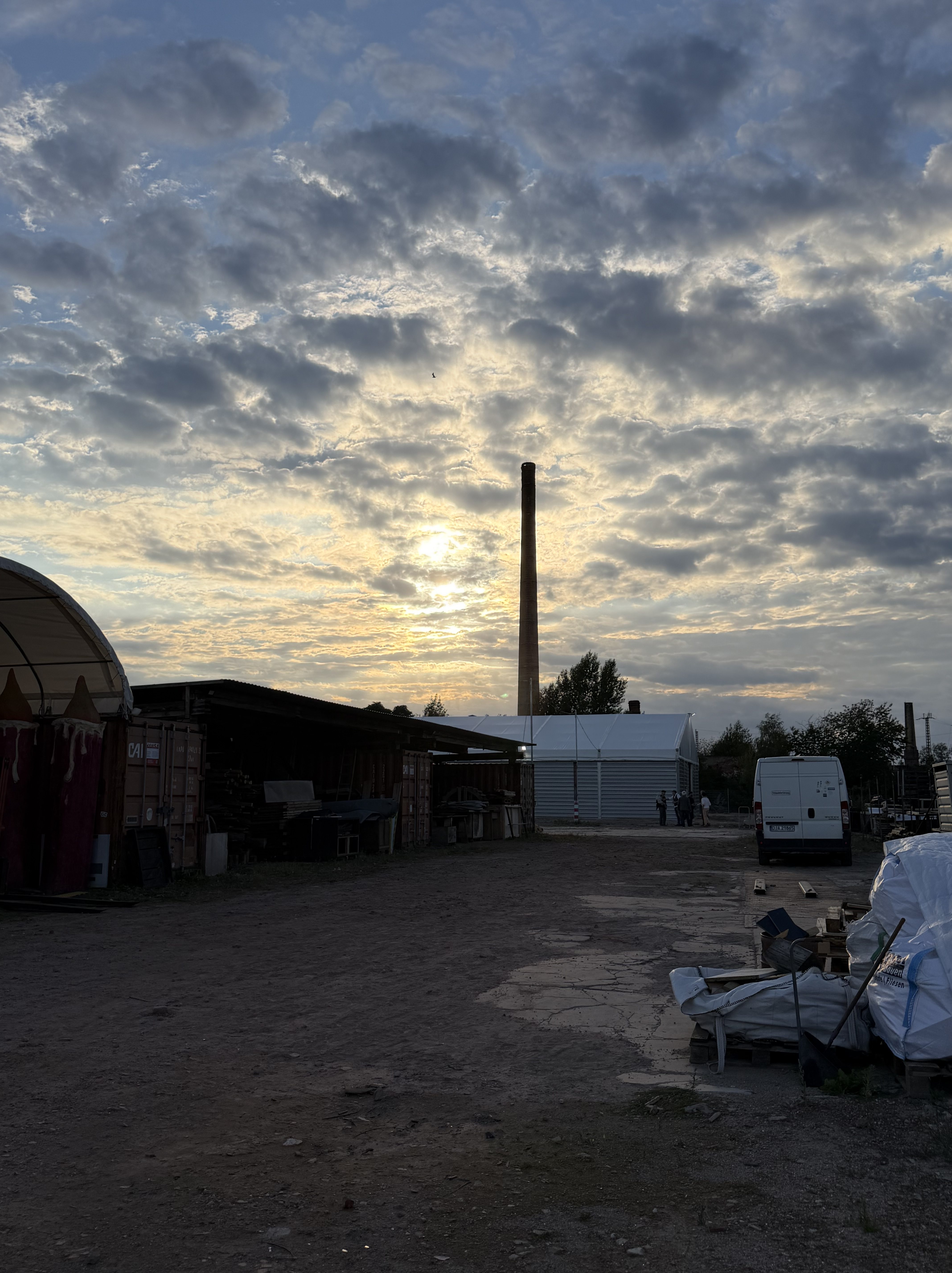 Industriegebiet bei Sonnenuntergang mit einem hohen Schornstein und Wolken am Himmel.